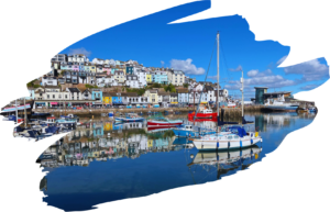 View of Brixham Harbour on a sunny day, boats in the water and colourful houses on the far side.